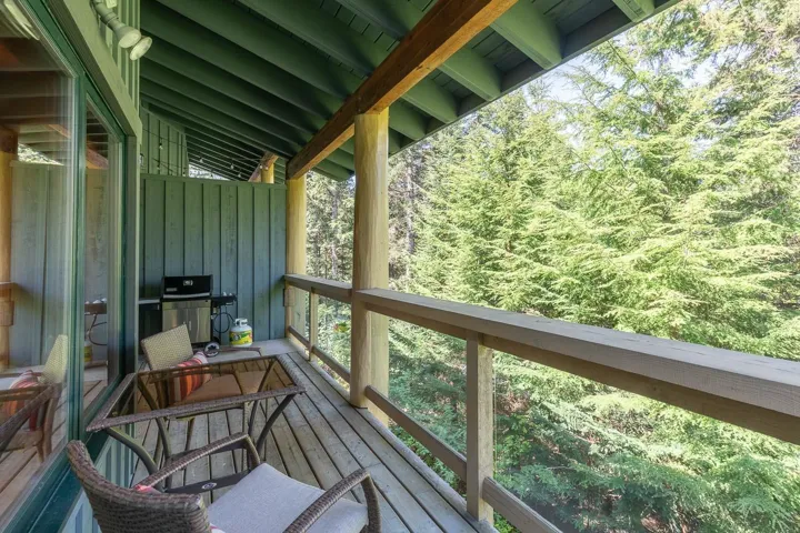 Covered balcony with wood-finish flooring, natural wood columns, and a railing featuring clear panels