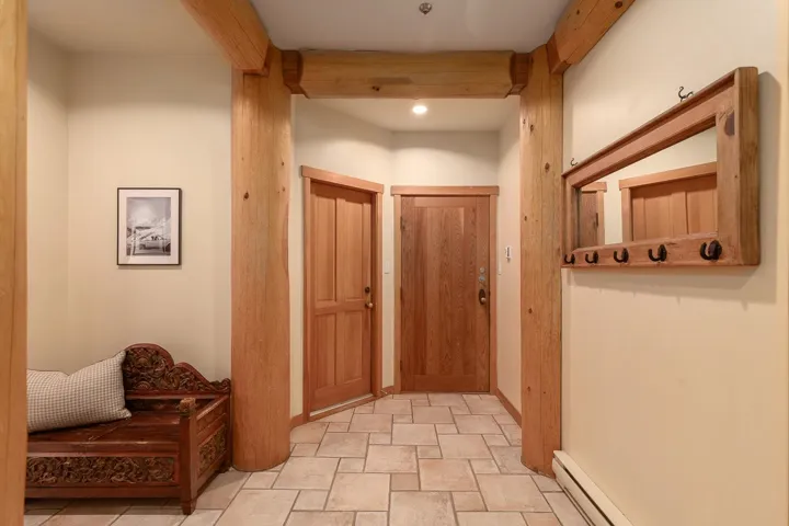 Entryway featuring robust timber-frame construction, paneled wood doors, beige tile flooring, light-toned wall paint, and recessed lighting