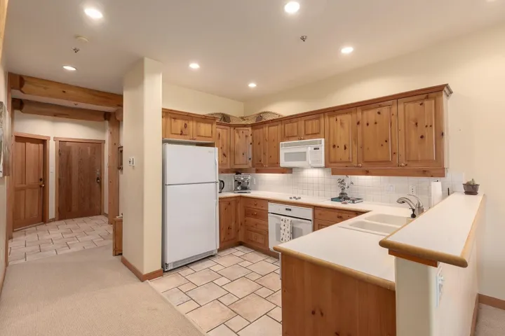Kitchen featuring knotty pine cabinetry, white appliances, square tile backsplash, and a double basin sink