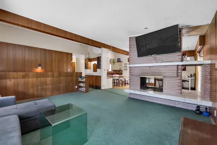 Unfurnished living room with wooden walls, carpet, and a brick fireplace