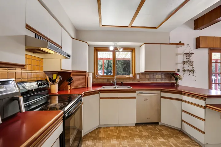 Two tone kitchen featuring black / electric stove, dishwasher, light floors, dark countertops, and decorative backsplash