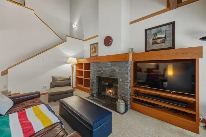 Living area featuring carpet flooring, a stone fireplace, a high ceiling, and stairway