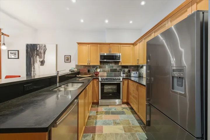 Kitchen with stainless steel appliances, dark stone countertops, tasteful backsplash, stone finish floors, and recessed lighting