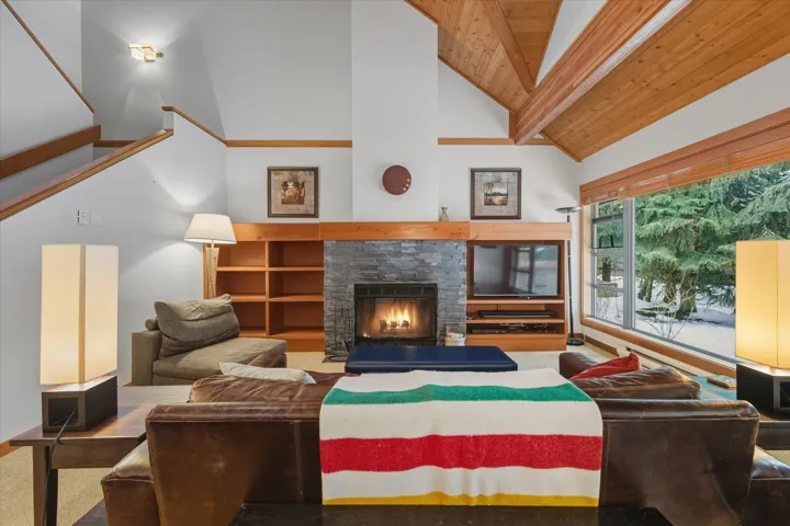 Living area featuring a stone fireplace, high vaulted ceiling, and a wooden ceiling with exposed beams