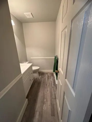 Half bathroom with vanity, baseboards, toilet, visible vents, and wood finished floors