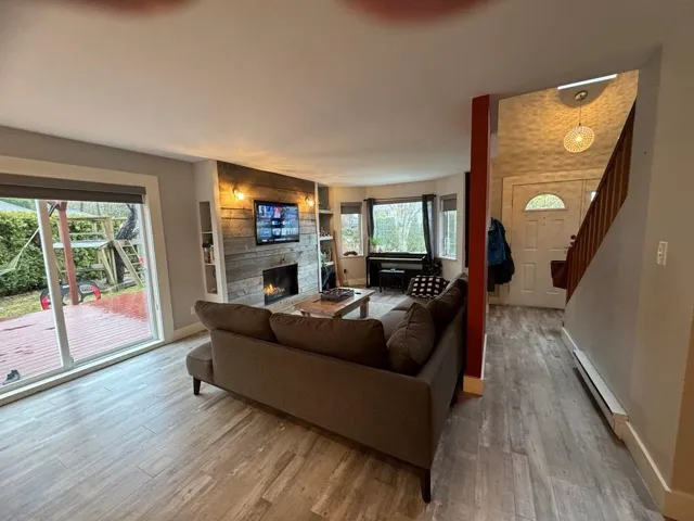 Living room featuring baseboards, baseboard heating, a fireplace, wood finished floors, and stairs