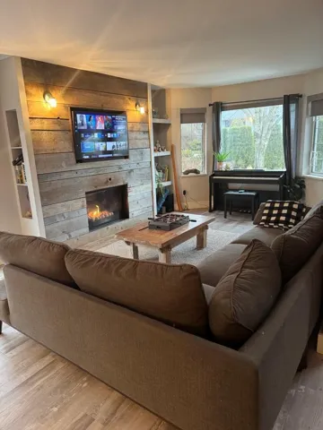 Living area with wooden walls, a lit fireplace, built in features, and wood finished floors