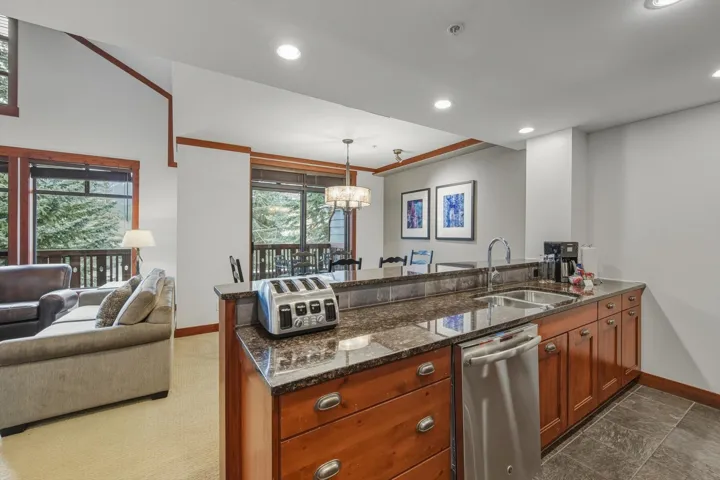 Kitchen featuring a peninsula, dark stone countertops, stainless steel dishwasher, hanging light fixtures, and open floor plan