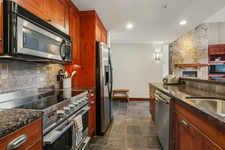 Kitchen featuring appliances with stainless steel finishes, dark stone countertops, dark stone finish floors, a fireplace, and recessed lighting