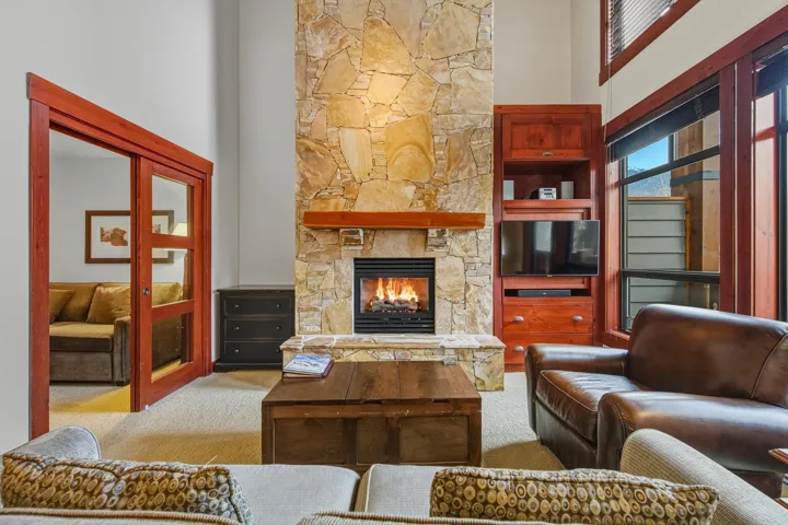 Carpeted living room with a stone fireplace and a towering ceiling