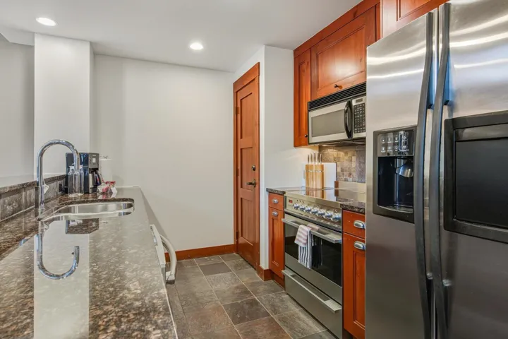 Kitchen featuring appliances with stainless steel finishes, dark stone counters, stone finish flooring, recessed lighting, and decorative backsplash
