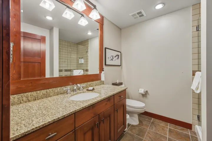 Bathroom with tiled shower, vanity, dark tile patterned flooring, and recessed lighting