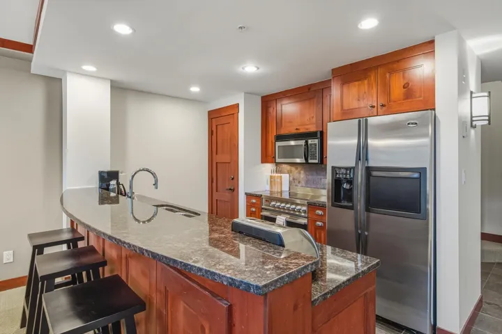 Kitchen featuring appliances with stainless steel finishes, a peninsula, brown cabinetry, a breakfast bar, and dark stone counters