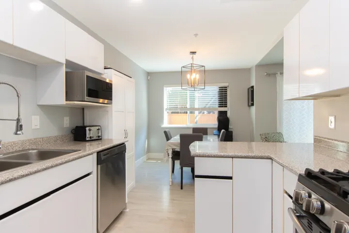 Kitchen with white cabinetry, stainless steel appliances, light wood-style flooring, decorative light fixtures, and light stone counters