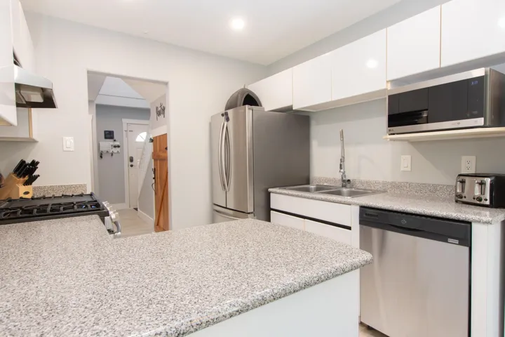 Kitchen featuring stainless steel appliances, white cabinets, light stone counters, a peninsula, and under cabinet range hood