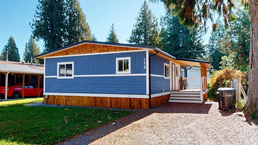 Exterior featuring blue horizontal siding, natural wood-finish shingle accents, wood-finish skirting, and an attached front deck with white railings
