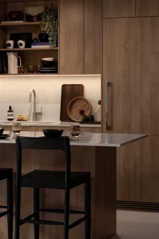 Integrated kitchen featuring wood-finish cabinetry, a large kitchen island with a light-toned countertop, and a recessed sink with a gooseneck faucet