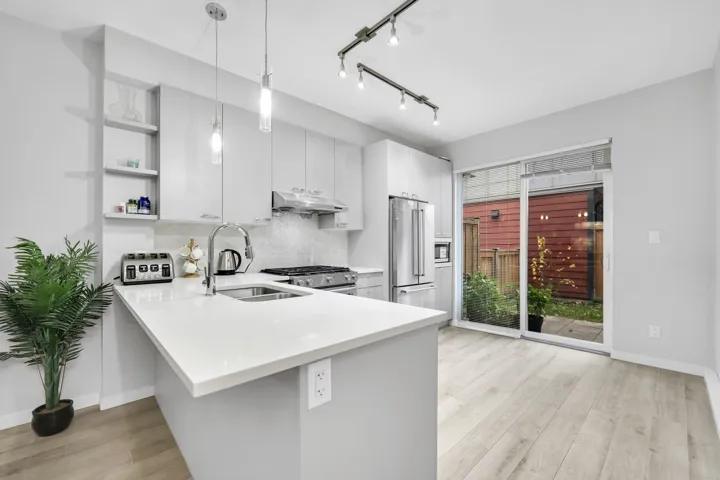 Kitchen with a peninsula, pendant lighting, stainless steel appliances, light wood finished floors, and white cabinets