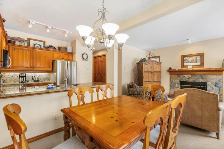 Dining room featuring a notable chandelier, light carpet, a stone fireplace, baseboards, and beamed ceiling
