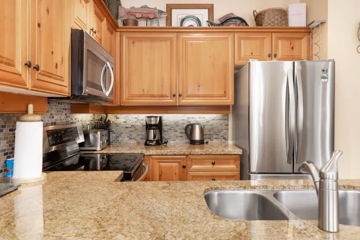 Kitchen with light stone countertops, a sink, stainless steel appliances, and backsplash