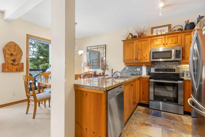 Kitchen with decorative backsplash, a sink, light stone countertops, appliances with stainless steel finishes, and brown cabinetry