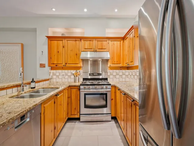 Kitchen with stainless steel appliances, light stone countertops, under cabinet range hood, light tile patterned floors, and recessed lighting