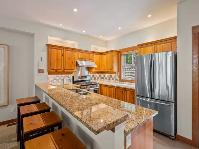 Kitchen featuring appliances with stainless steel finishes, backsplash, a kitchen bar, a peninsula, and light stone counters