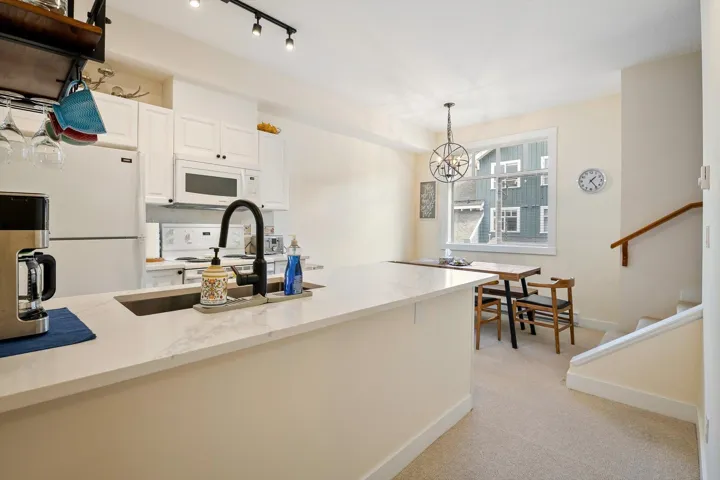 Kitchen with white appliances, white cabinets, light stone counters, light colored carpet, and hanging lights