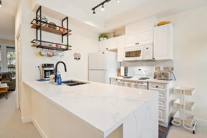 Kitchen with a peninsula, white cabinets, white appliances, light stone countertops, and decorative backsplash