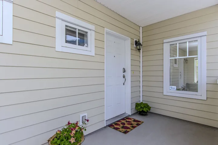 Entryway featuring a white paneled door, two white-framed windows with grilles, cream-colored horizontal siding, and a black outdoor wall lantern