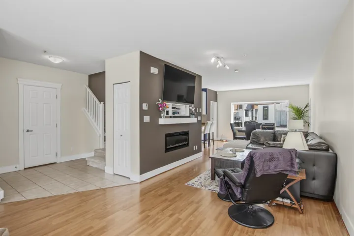 Bright living area featuring wood-finish flooring, a built-in electric fireplace with a white mantel, and a staircase with white balusters