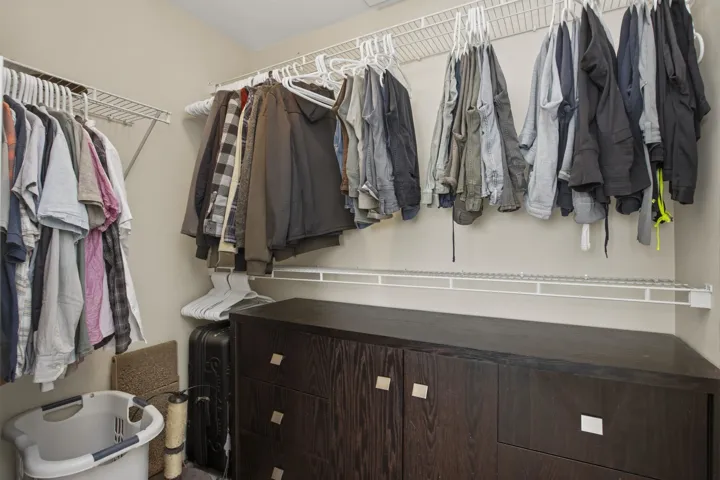 Walk-in closet featuring built-in wire shelving, a dark wood-finish storage unit with drawers and cabinet doors, and light-toned walls