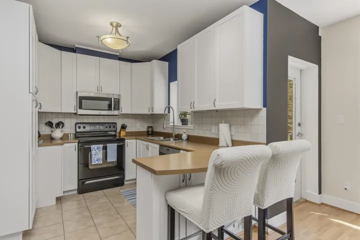 Kitchen featuring extensive white cabinetry, a built-in microwave, tiled backsplash, light-toned countertops, and an integrated breakfast bar with seating