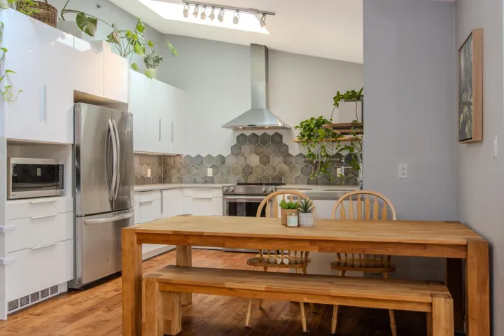 Kitchen with appliances with stainless steel finishes, wall chimney range hood, backsplash, white cabinets, and light wood-style floors