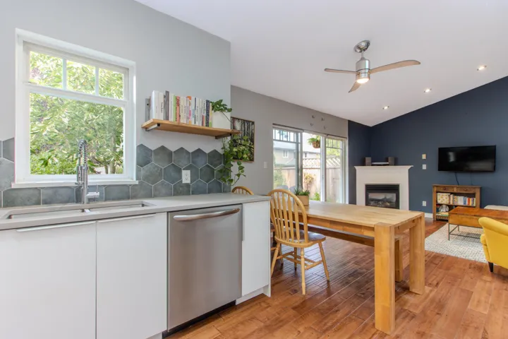 Kitchen featuring white cabinetry, stainless steel dishwasher, a glass covered fireplace, light wood-type flooring, and lofted ceiling