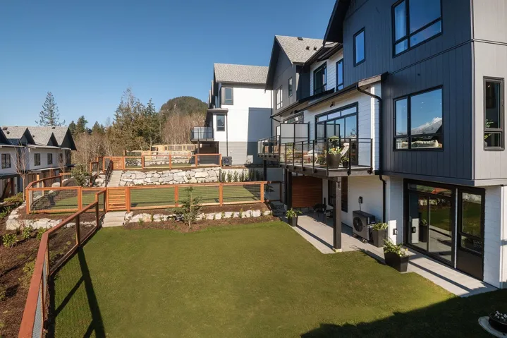 Contemporary exterior with multi-level design, glass panel balcony, wood fencing, tiered landscaping, and turf backyard areas