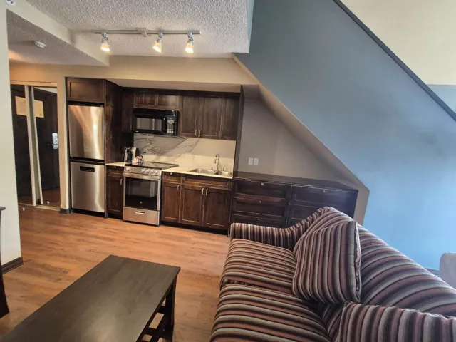Kitchen with dark brown cabinets, light countertops, stainless steel appliances, light wood-style flooring, and a textured ceiling