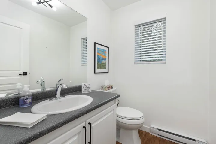 Half bathroom featuring baseboard heating, wood finished floors, and vanity