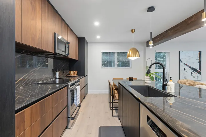 Kitchen featuring modern cabinets, dark stone countertops, appliances with stainless steel finishes, pendant lighting, and light wood-type flooring