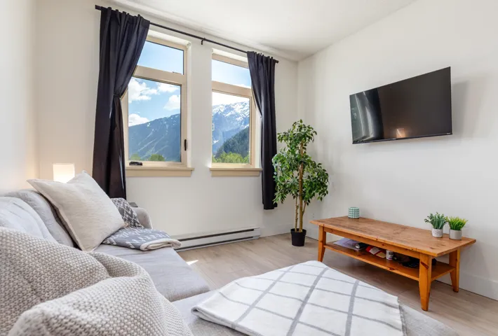 Living area featuring two large windows with mountain scenery, light wood-finish flooring, and white walls