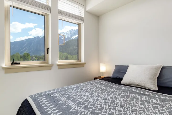 Dual windows with mountain and tree scenery, white window blinds, and light-toned window sills