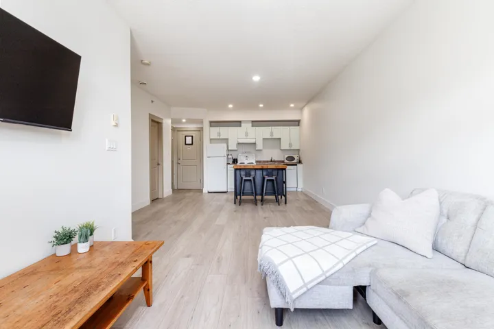 Open-concept living space featuring wood-finish flooring, recessed lighting, white walls, and a contemporary kitchen with light-toned cabinetry and a dark-toned island