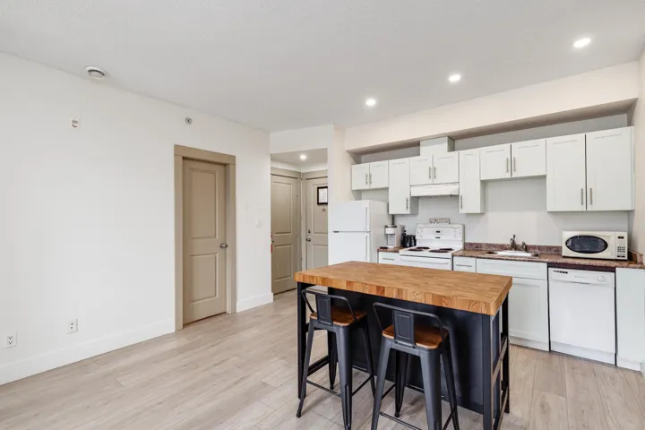 Open-concept kitchen featuring white cabinetry, a built-in electric range, a stainless steel sink, and a contrasting island with a butcher block countertop