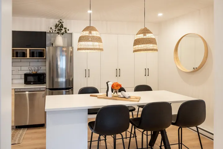 Modern kitchen and dining area featuring a spacious white countertop island, stainless steel appliances, white subway tile backsplash, and light wood-finish flooring