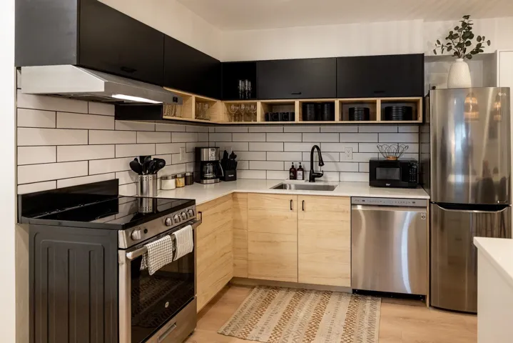 Contemporary kitchen featuring two-tone cabinetry with black upper cabinets and light wood-finish lower cabinets, stainless steel appliances, a subway tile backsplash, and light-toned countertops