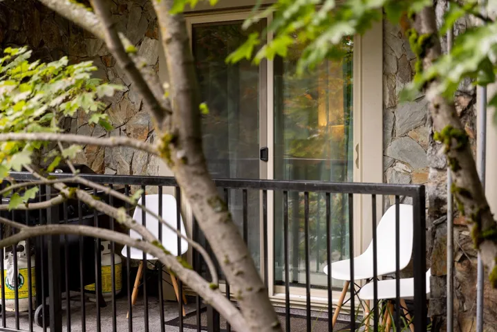 Exterior balcony featuring a sliding glass door, stone veneer siding, and black metal railings