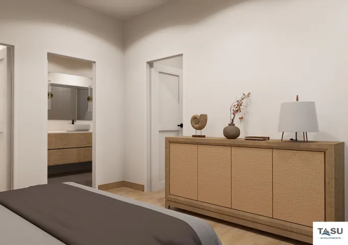 Bright bedroom featuring light wood-finish flooring and a doorway revealing a bathroom with a floating vanity