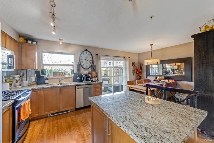 Kitchen with light stone countertops, light wood-style floors, brown cabinetry, stainless steel appliances, and a sink