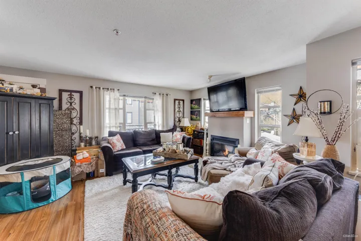 Living room with a textured ceiling, a glass covered fireplace, wood finished floors, and a healthy amount of sunlight