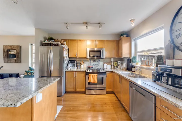 Kitchen with light stone counters, a sink, stainless steel appliances, light wood finished floors, and decorative backsplash